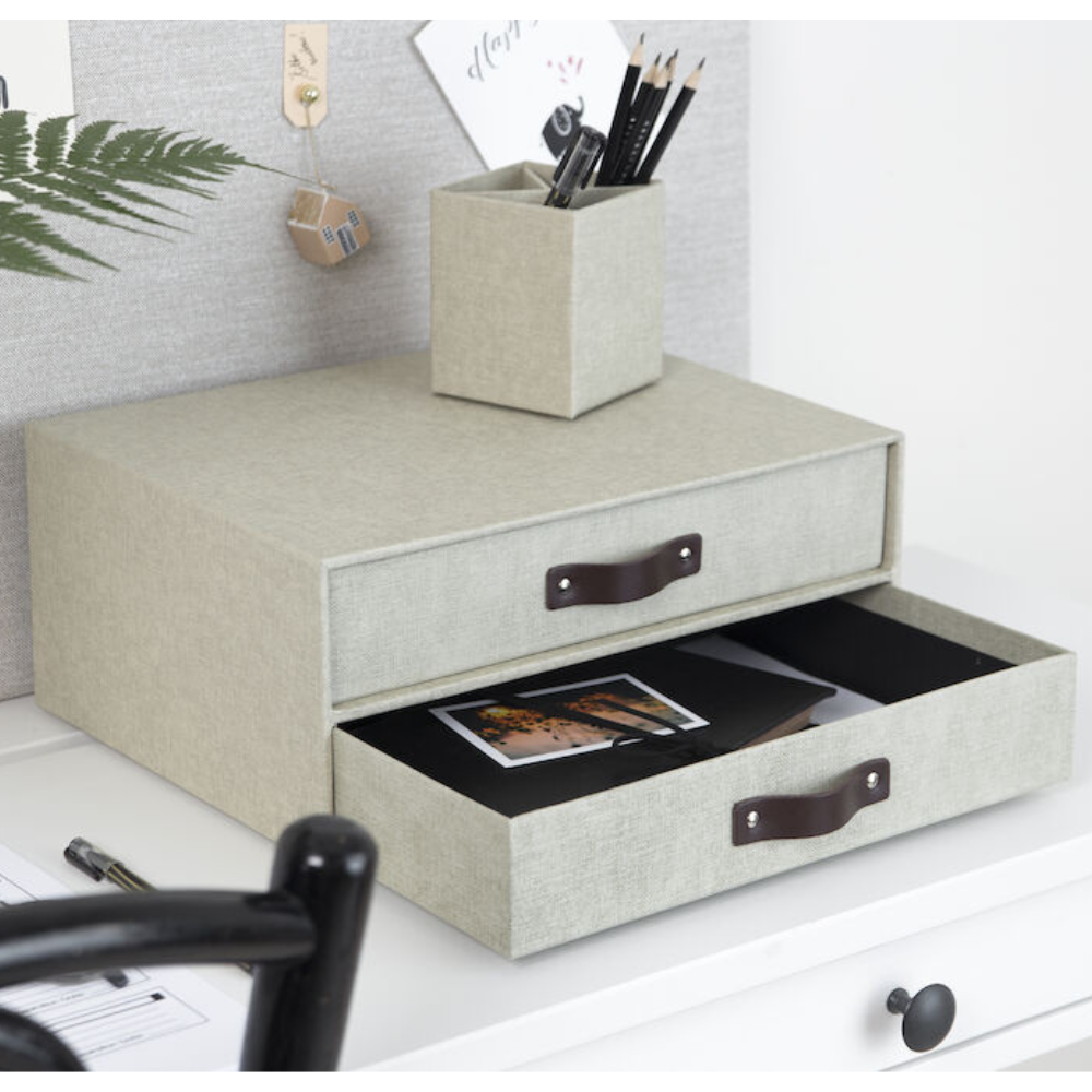 Op een wit bureau staat een Bigso BIRGER ladekastje met twee vakken van linnen canvas. De onderste lade is open en je kunt de foto’s erin zien. Bovenop staat een bijpassende pennenhouder met pennen en potloden.