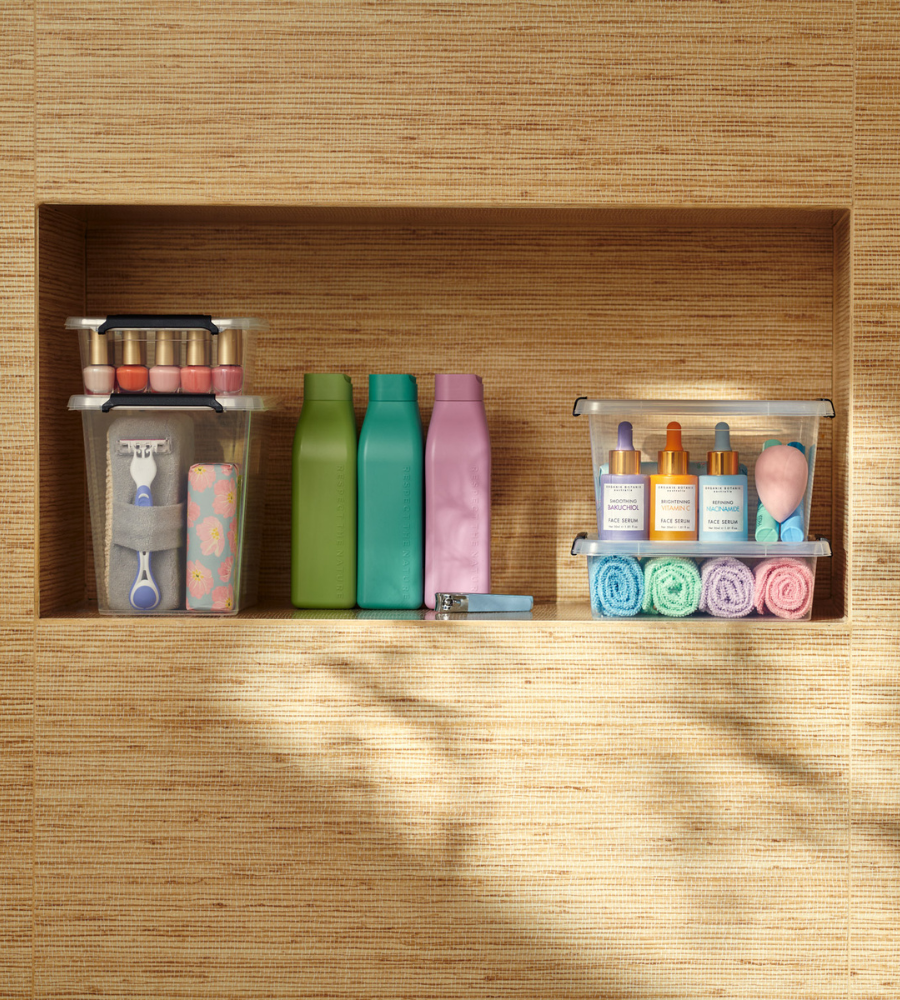 Op drie badkamerplanken worden de toiletartikelen netjes opgeborgen in de Orplast SimpleStore Box - 29x20x12 cm (4,5 l): nagellak, scheermesjes, huidverzorgingsserum, make-upsponsjes, washandjes en flesjes tegen een geweven wand.