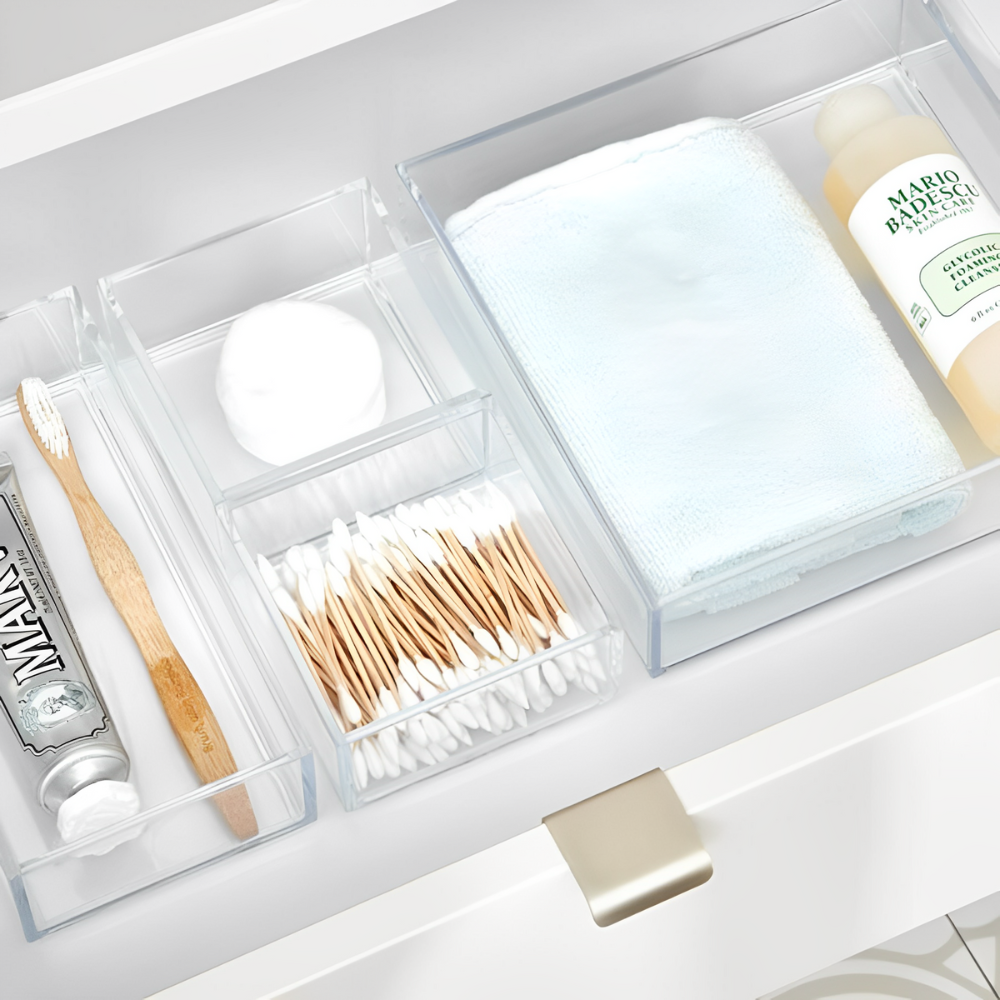 In een badkamerlade liggen een bamboe-tandenborstel, tandpasta, wattenbolletjes en Mario Badescu-reinigingsgel overzichtelijk gerangschikt in doorzichtige acrylbakjes uit de iDesign-lade-organizer-set CLARITY (5-delig).