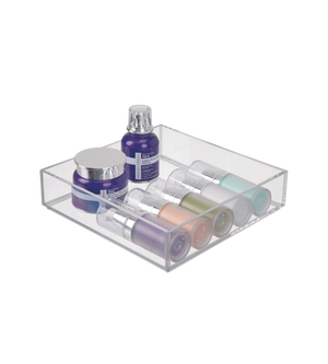 Een doorzichtige bak met kleurrijke cosmeticaflesjes en -potjes, op een witte ondergrond.