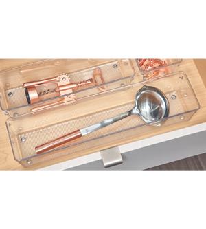 Een zilveren pollepel met koperen handvat en een koperen kurkentrekker zijn netjes opgeborgen in doorzichtige bakjes uit de iDesign-lade-organizer-set LINUS - HOOG (5-delig) in een lichte houten lade.