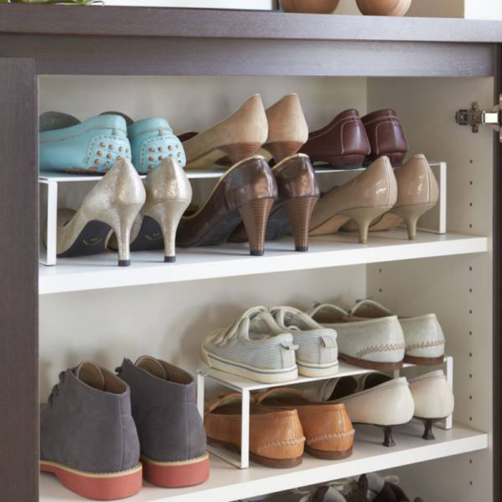 Een overzichtelijk georganiseerde YAMAZAKI FRAME uitschuifbare schoenenkast – wit – met planken vol dames- en herenschoenen, zoals hoge hakken, loafers, platte schoenen en sneakers, die in rijen op en onder de slanke, uitschuifbare plank zijn gerangschikt.