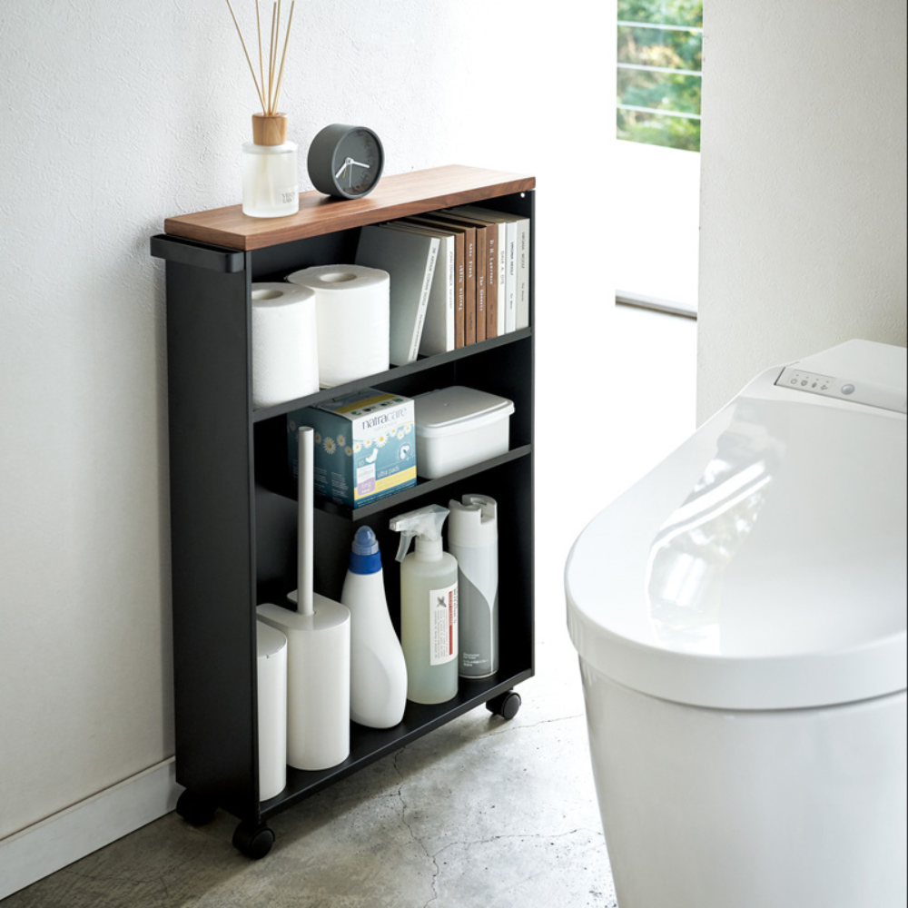 De TOWER opbergwagen met handgreep van YAMAZAKI in zwart biedt ruimte voor toiletpapier, schoonmaakmiddelen en nog veel meer – ideaal naast het moderne witte toilet in de lichte badkamer.