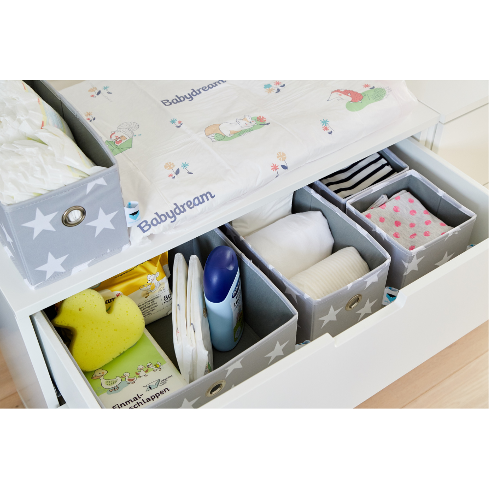 Een overzichtelijke commode met de Love it Store it STAR Organizer Grijs - set van 5 stuks voor het netjes opbergen van luiers, vochtige doekjes, lotion, een gele spons, babykleertjes en doekjes onder een speels geïllustreerd aankleedkussen in stervormig geplaatste bakjes.