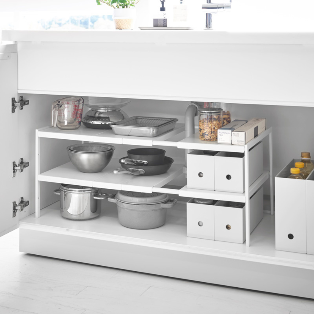 Open witte TOWER-rek, uitschuifbaar - wit van YAMAZAKI, met georganiseerde, in hoogte verstelbare planken voor het flexibel opbergen van potten, pannen, potten met pasta, voedselbakjes en schoonmaakmiddelen, overzichtelijk gerangschikt aan de rechterkant.