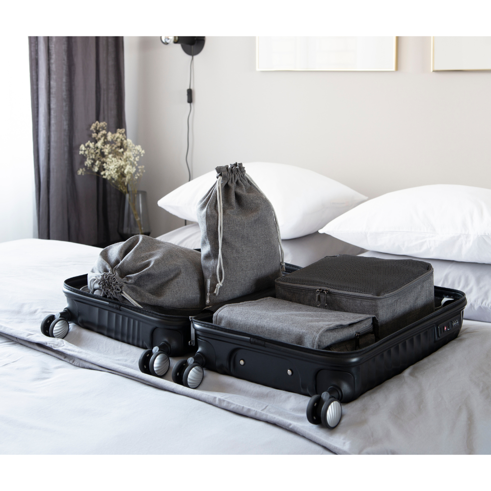 Een zwarte koffer staat open op een opgeruimd bed, gevuld met grijze opbergkubussen, zakjes en de Bigso TRAVEL waszak Grijs - 2 stuks - ideaal voor elke reis. Gedempt licht, witte kussens en een minimalistische inrichting maken het plaatje compleet.