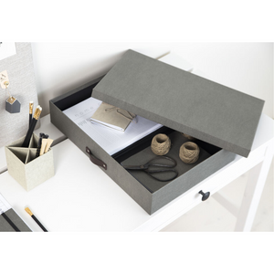 Een grijze Bigso SVERKER opbergbox A3 van canvas staat met half geopend deksel op een wit bureau. Binnenin: notitieboekjes, touw en een schaar – ideaal voor het opbergen van documenten in een georganiseerde werkplek.