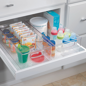 In een opgeruimde keukenlade staat de iDesign keukenset MINI (5-delig) met overzichtelijke, stapelbare opbergsystemen voor babyvoeding, snacks, zakjes en flesjes met gekleurde doppen. Witte lades en kastjes benadrukken de opgeruimde uitstraling.