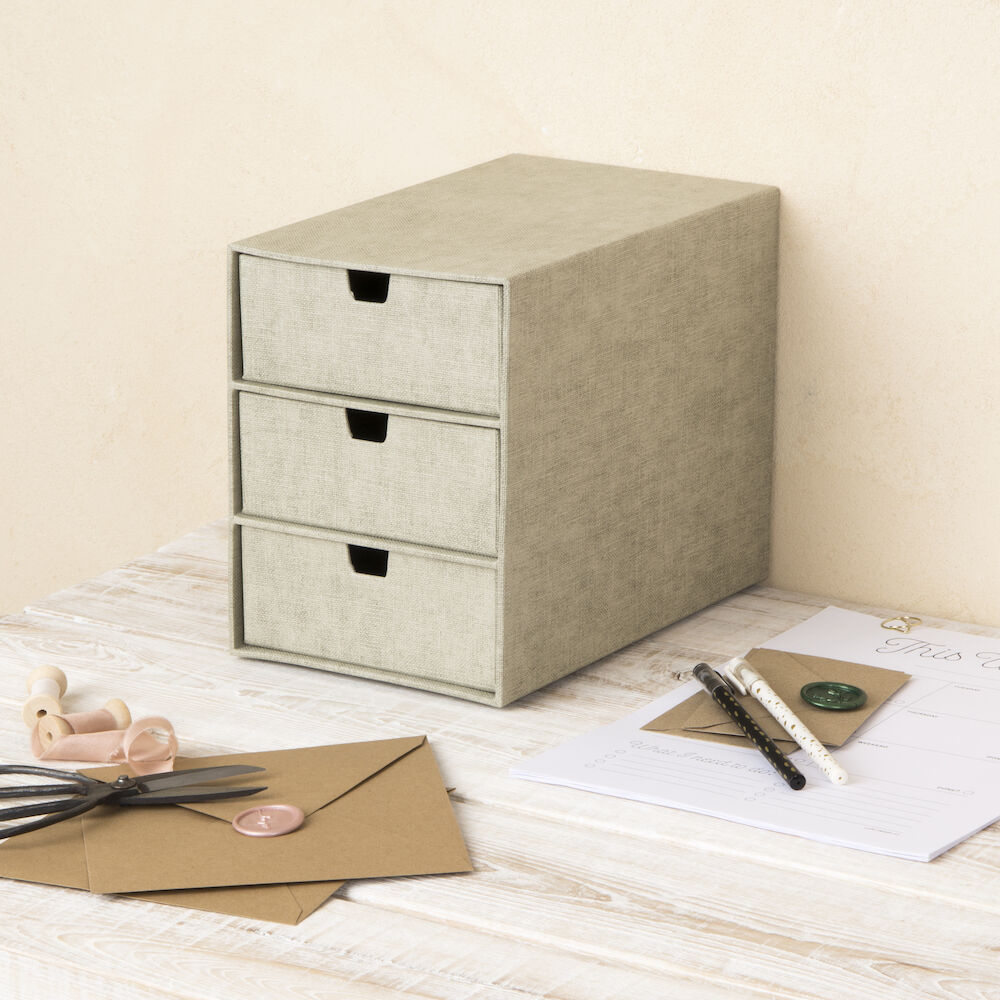 De INGRID-ladekast met 3 vakken – linnen canvas van Bigso staat op een lichte houten tafel en helpt je bij het organiseren van je kantoor met bruine enveloppen, briefpapier, een pen, een wasstift, een lakzegel en een schaar.