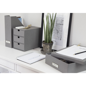 Een opgeruimd wit bureau met de Bigso OSKAR opbergdoos A4 – grijs, een potplant, ingelijste kunst, een spiraalnotitieboekje en een blok met een takenlijst zorgt voor een georganiseerde, moderne werkplek.