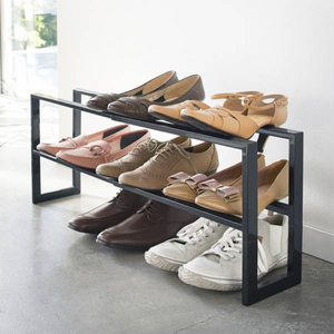 Een schoenenrek met verschillende schoenen, dat op een betonnen vloer naast een witte muur staat.