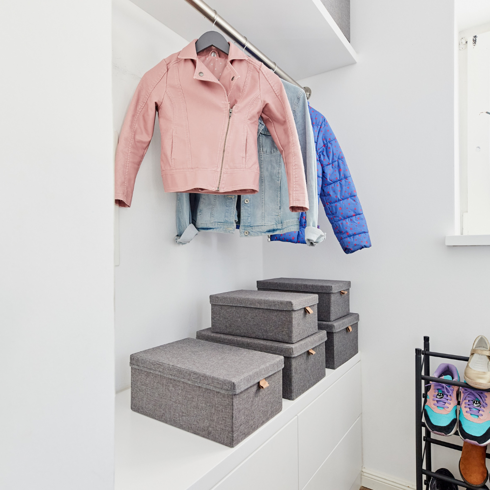 Een opgeruimde kledingkast met een roze jasje, een spijkerhemd en een blauw jasje hangt boven de Love it Store it PREMIUM opbergdozen met deksel in grijs – set van 5 stuks. Schoenen en sneakers staan netjes op een zwart schoenenrek aan de rechterkant – perfect voor een opgeruimd huis.