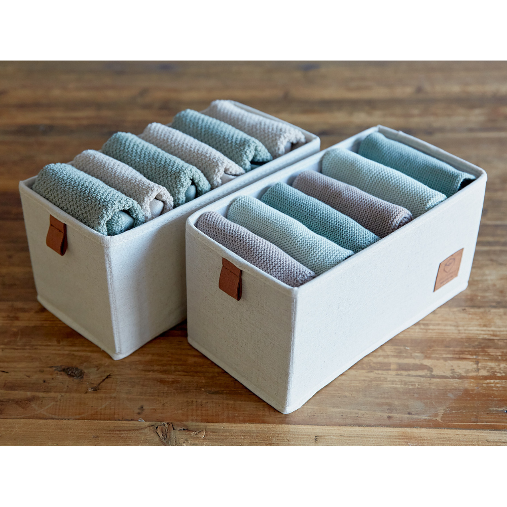 Twee PREMIUM-opbergers met 6 vakken, smal, beige – set van 2 stuks van Love it Store it, gevuld met keurig opgerolde blauwe en grijze handdoeken, staan op een houten ondergrond. Elke opbergbak heeft een bruin, leerachtig label voor een stijlvolle touch.