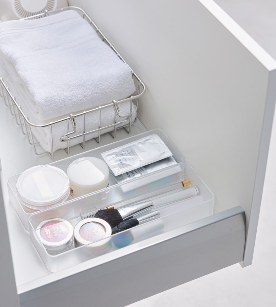 Een opgeruimde witte lade met de YAMAZAKI TOWER lade-organizer wit L (set van 2 stuks), een metalen mandje met opgevouwen handdoekjes en een doorzichtig bakje voor make-upborstels en beautyproducten – ideaal om je lades te organiseren.