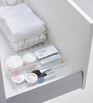 Een opgeruimde witte lade met de YAMAZAKI TOWER lade-organizer wit L (set van 2 stuks), een metalen mandje met opgevouwen handdoekjes en een doorzichtig bakje voor make-upborstels en beautyproducten – ideaal om je lades te organiseren.