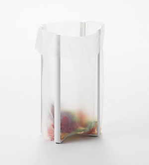 Een doorzichtige plastic zak hangt open aan een YAMAZAKI TOWER multifunctionele keukenrek - wit, met kleurrijke etensresten op de bodem, tegen een eenvoudige witte achtergrond.
