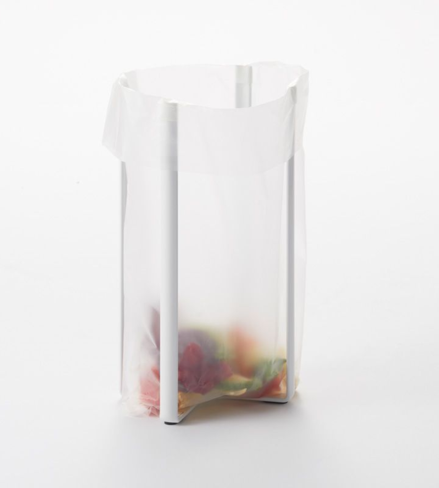 Een doorzichtige plastic zak hangt open aan een YAMAZAKI TOWER multifunctionele keukenrek - wit, met kleurrijke etensresten op de bodem, tegen een eenvoudige witte achtergrond.
