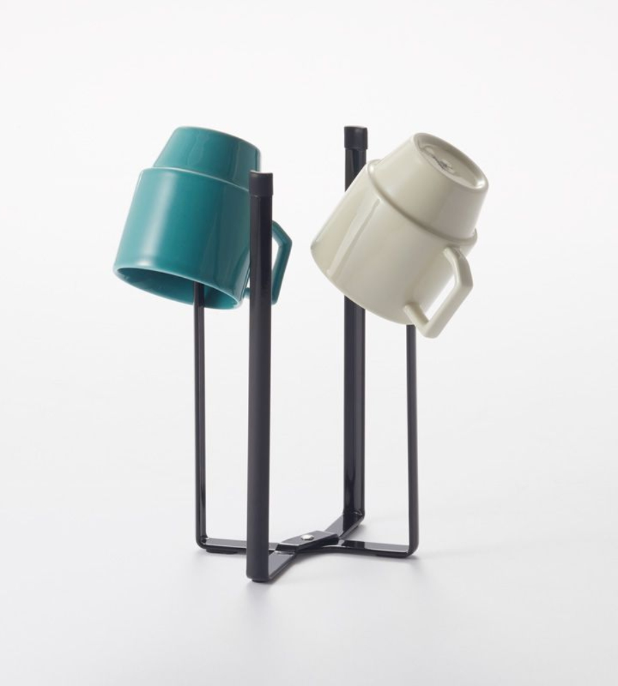 Twee kopjes, een blauwgroene en een beige, hangen ondersteboven aan de zwarte YAMAZAKI TOWER multifunctionele keukenhouder tegen een eenvoudige witte achtergrond.