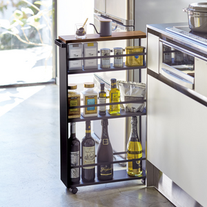 De YAMAZAKI TOWER keukentrolley met handgreep in zwart is een slanke metalen trolley met vier schappen, ideaal voor olie- en azijnflessen, kruidenpotjes en nog veel meer naast het moderne keukenkastje bij het raam.
