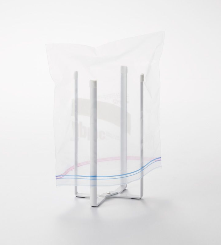 De YAMAZAKI TOWER multifunctionele keukenhouder - wit houdt een doorzichtig plastic zakje met ritssluiting open. Deze opvouwbare keukenhouder met vier poten maakt het werk makkelijker en wordt getoond tegen een eenvoudige witte achtergrond.