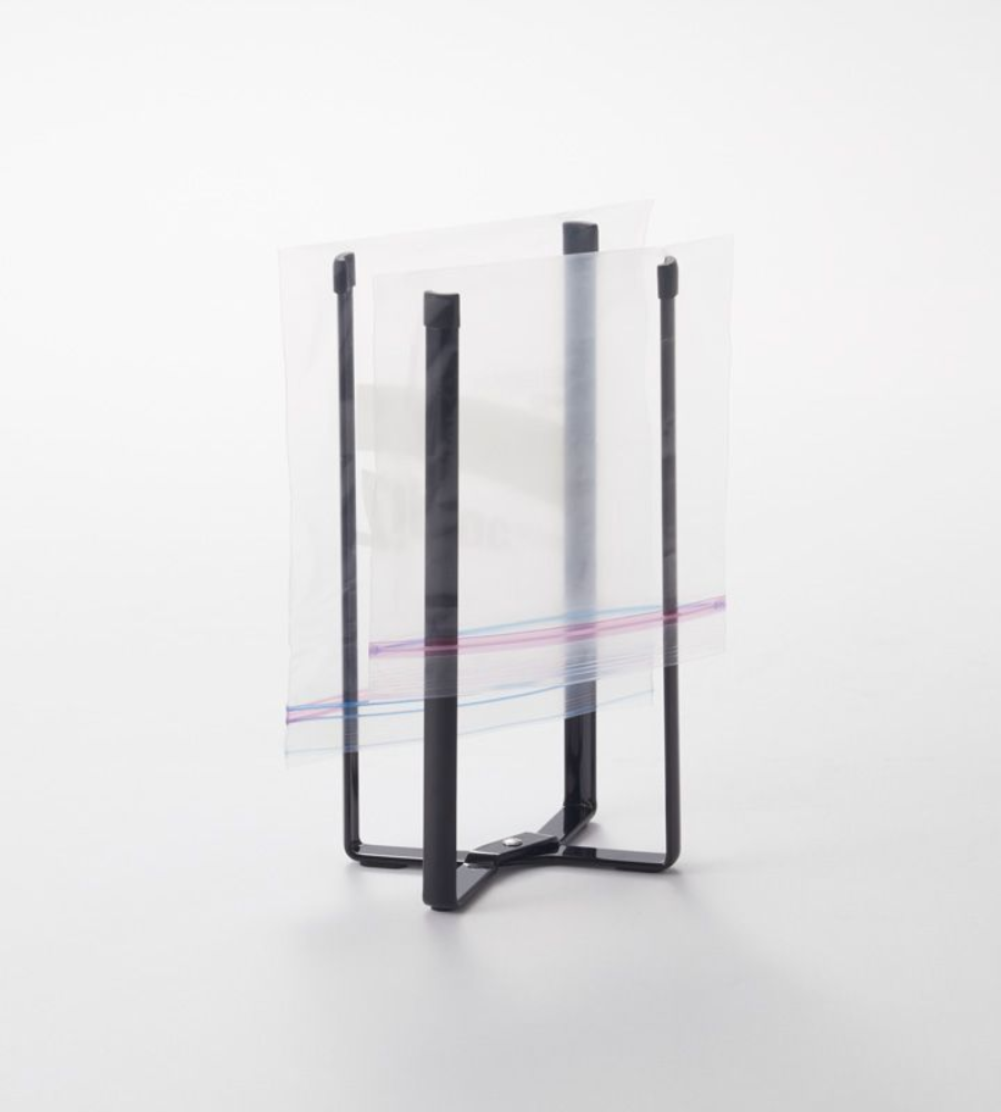 De YAMAZAKI TOWER multifunctionele keukenhouder - zwart houdt een open Zip-Top-zak rechtop, zodat je hem makkelijk kunt vullen. Hij staat afgebeeld op een strak wit oppervlak.
