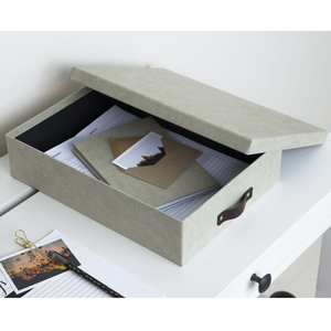 Een grijze Bigso OSKAR opbergdoos A4 – linnen canvas met een gedeeltelijk open deksel staat op een witte tafel en is bedoeld voor het opbergen van documenten en enveloppen – ideaal voor het ordenen van papierwerk in je thuiskantoor.