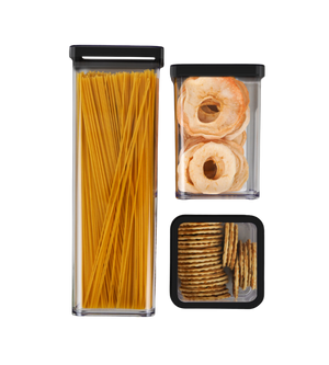 Drie doorzichtige bakjes met zwarte deksels bevatten spaghetti, appelringen en crackers tegen een neutrale achtergrond.