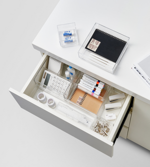 In een open bureaulade zorgt de BNB x VCN SLIDE lade-organizer KLAR – diverse maten ervoor dat pennen, markeerstiften, rekenmachines, plakband, gummen, notitieboekjes en paperclips netjes gesorteerd blijven; bovenop liggen een gesloten notitieboekje en gummen. Perfect om lades te organiseren.