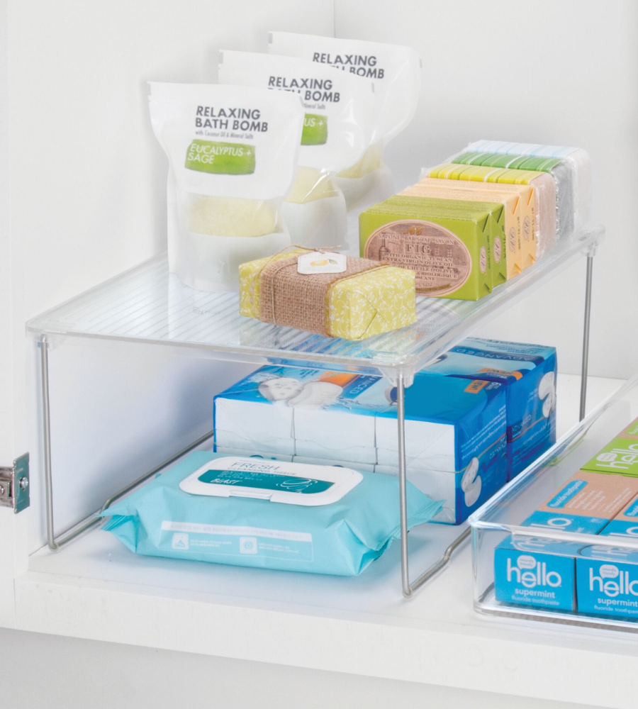Een overzichtelijke kast met badbruisballen, zeepjes en vochtige doekjes op en onder de iDesign LINUS - rekinzetstuk KLAR, plus een doorzichtig schap met tandpastablikjes voor een optimaal ruimtegebruik.
