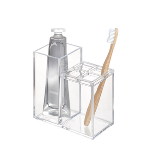 De iDesign CLARITY - Kosmetik Organizer KLAR II, een doorzichtige acrylhouder, biedt overzichtelijk plaats aan een tube tandpasta en een bamboe-tandenborstel met witte borstelharen – een ideale opbergoplossing voor in de badkamer tegen een strakke witte achtergrond.