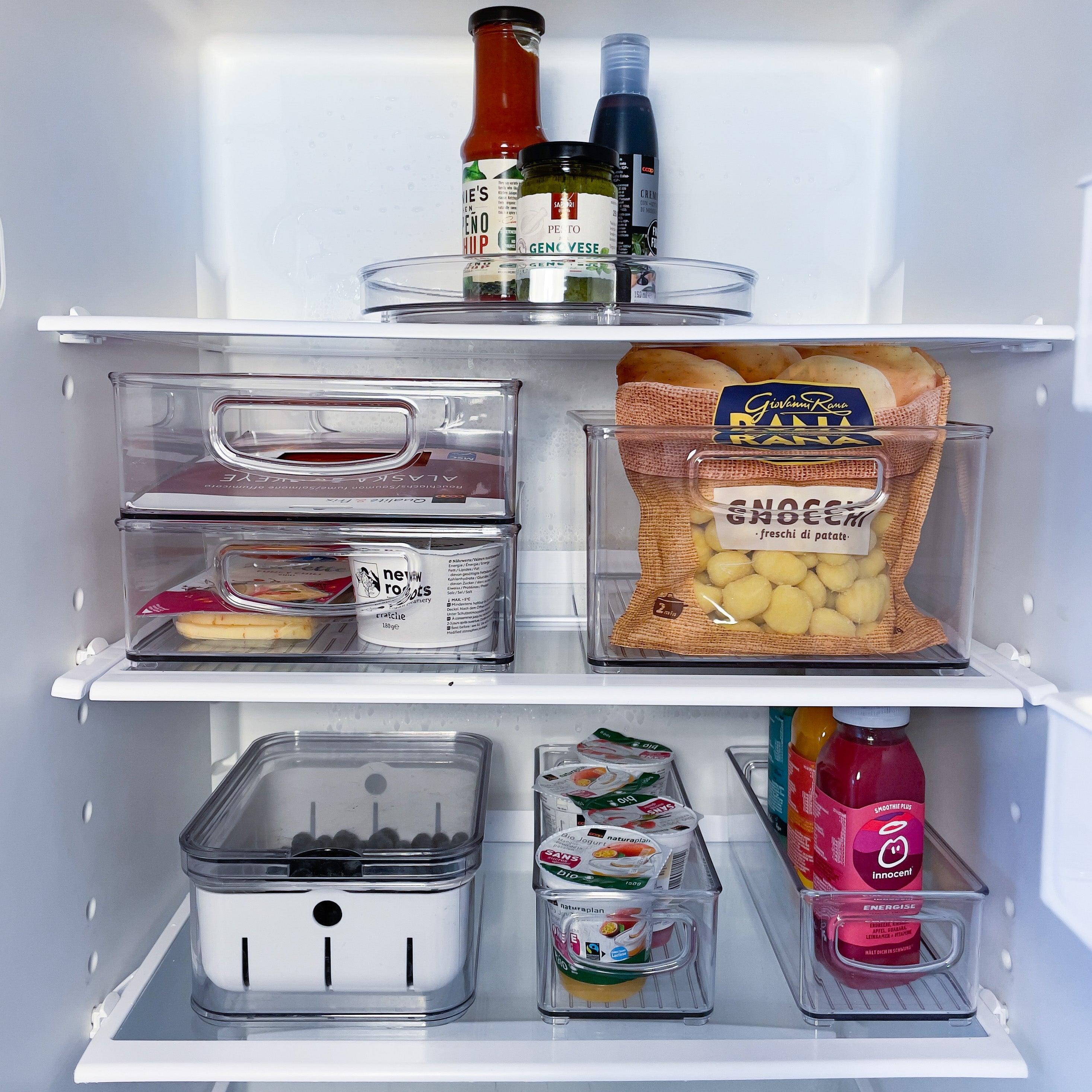 Koelkast met netjes geordende etenswaren in plastic bakjes: sauzen boven, gnocchi in het midden, yoghurt onderaan.