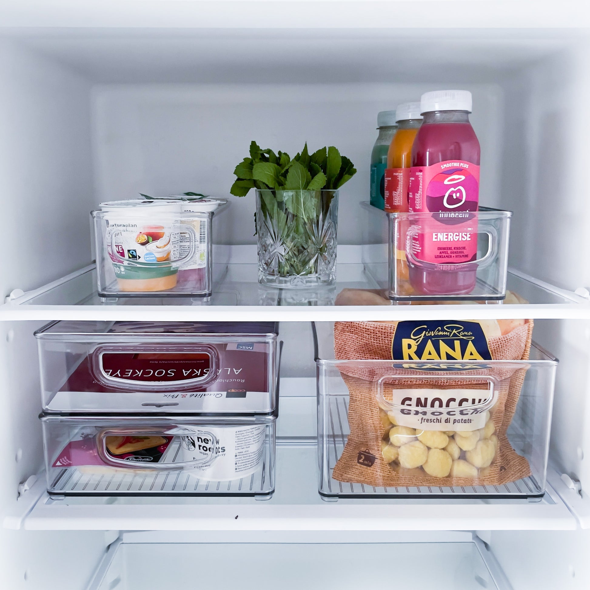 Een koelkastrek met yoghurtbekers, sapflesjes, plakjes kaas en vleeswaren – netjes opgeborgen in de koelkastset MINI (5-delig), een stapelbare opbergset van iDesign.