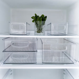 In een opgeruimd koelvak staat de iDesign-koelkastset MINI (5-delig): vijf stapelbare bakjes, allemaal leeg behalve een glazen pot in het midden met verse groene kruiden.
