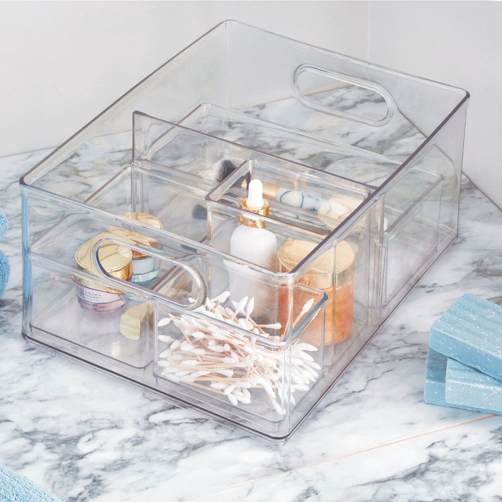 De iDesign HOME EDIT opbergbak TRANSPARANT met 2 vakken (25,4 x 34,3 x 15,2 cm) houdt wattenstaafjes, druppelflesjes en cosmetica netjes op het marmeren blad naast blauwe handdoeken en zeepjes – stapelbaar, met uitneembaar tussenschot.