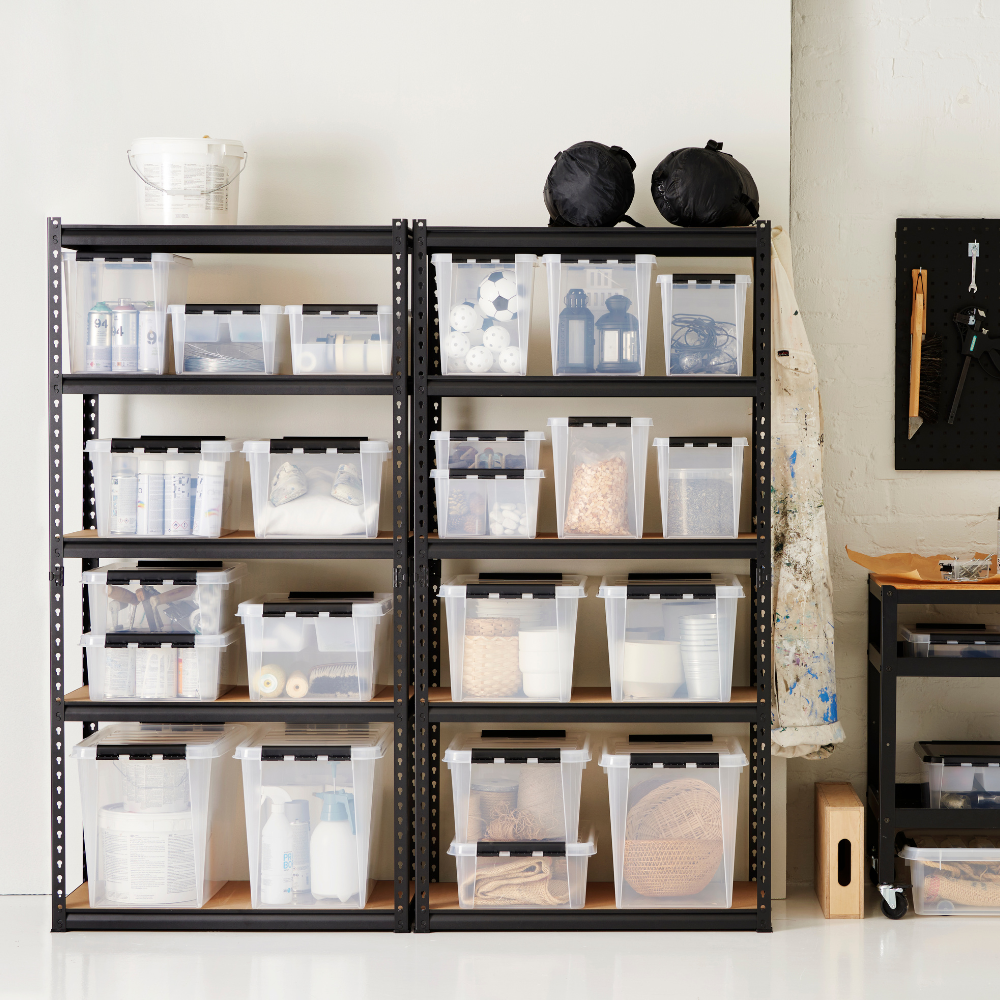 Op de metalen rekken staan Orthex SmartStore Box KLAR 40x30x11 cm (7,5 l), BPA-vrij en netjes geordend met knutselmateriaal. Vlakbij staan een werkschort, een gereedschapsrek en een rolwagen met nog meer materiaal.