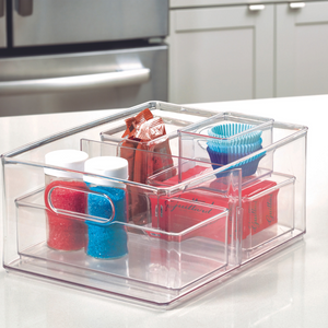 Een HOME EDIT - doorzichtige opbergbak met 2 vakken van iDesign (25,4 x 34,3 x 15,2 cm) houdt cakemixen, cupcakevormpjes, toppings en hagelslag netjes geordend op het aanrecht; op de achtergrond zie je de koelkast en witte kasten.