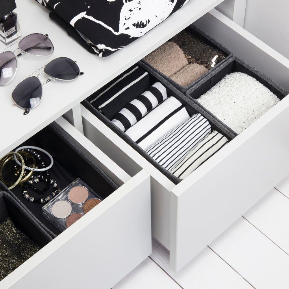 Lades met kleding, accessoires en een brillenkoker, met daarnaast een zonnebril en nagellak op een wit oppervlak.