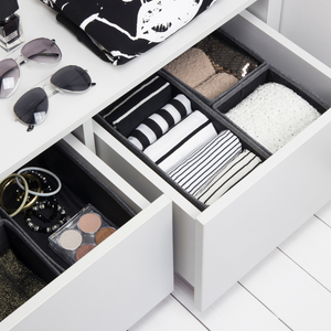 Lades met kleding, accessoires en een brillenkoker, met daarnaast een zonnebril en nagellak op een wit oppervlak.
