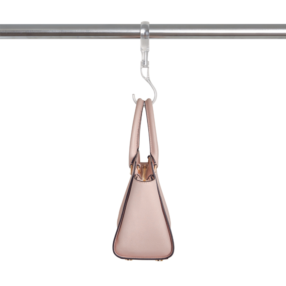 Aan de iDesign HOME EDIT - S-haak TRANSPARANT hangt een beige handtas aan een metalen stang tegen een witte achtergrond – ideaal om je kledingkast ruimtebesparend op te ruimen.