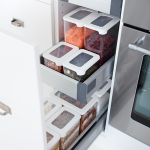 Een Orthex SmartStore-set met doorzichtige en witte voorraadpotten, stuk voor stuk luchtdicht afgesloten en gevuld met granen, linzen, bonen en pasta, staat overzichtelijk gerangschikt op uittrekbare planken in een keukenkast naast de oven.