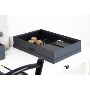 Een SVERKER opbergbox A3 in zwart canvas van Bigso staat op een wit bureau, waarop garenklossen, scharen en notitieboekjes netjes zijn opgeborgen. Een zwarte stoel en een potlood maken het minimalistische, overzichtelijke tafereel compleet.