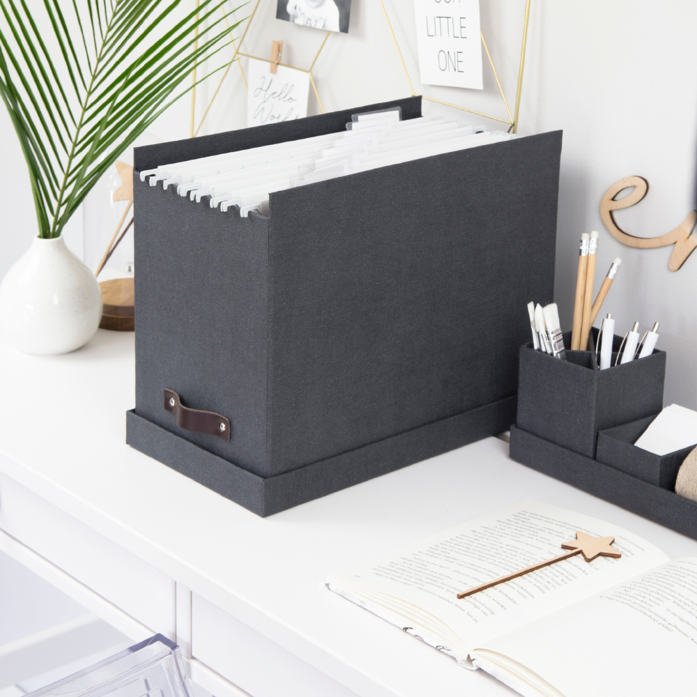 Grijze opbergbox met hangmappen op een wit bureau, omringd door decoraties.