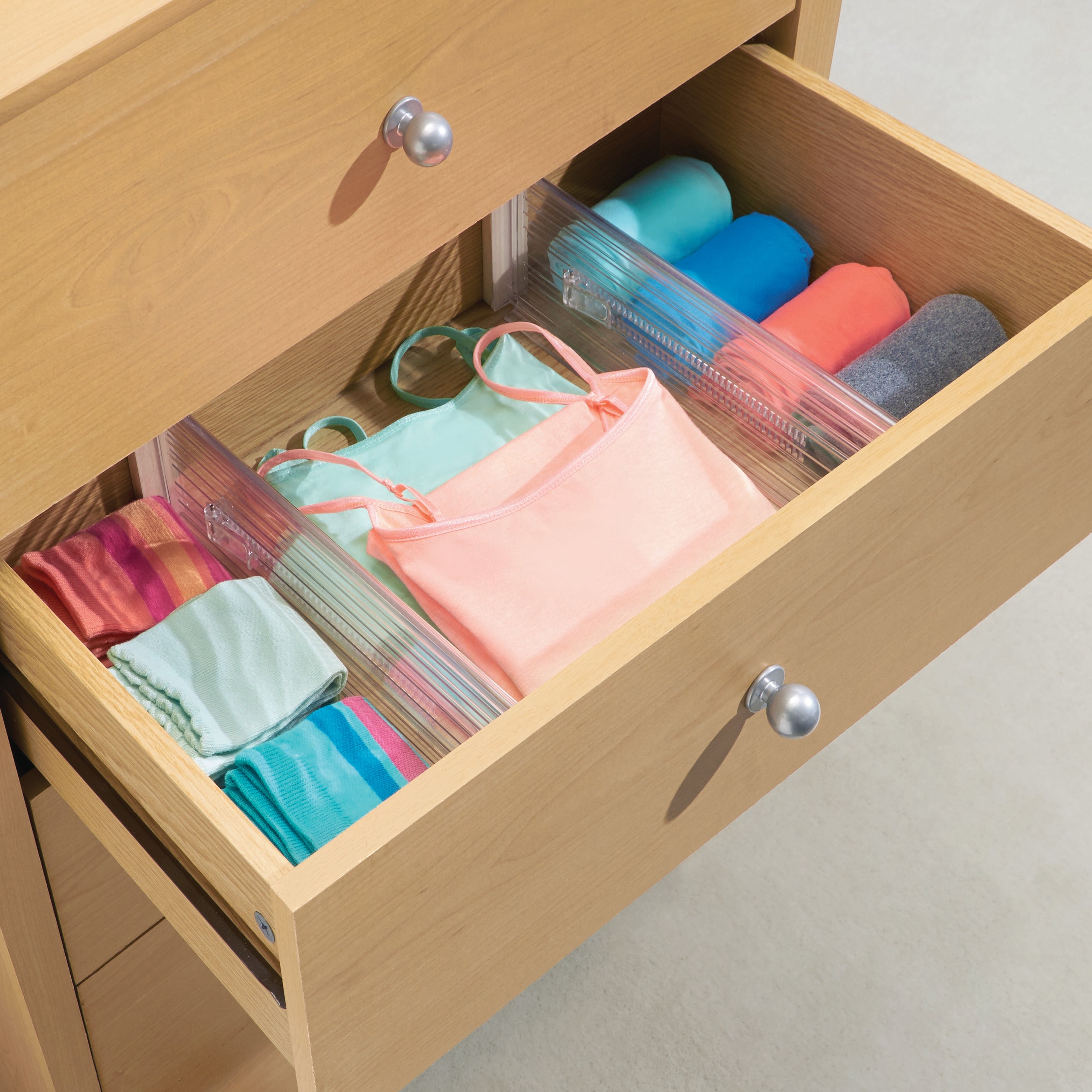 Houten lade met twee vakken, gevuld met opgevouwen en opgerolde kleding, in een lichte ruimte.
