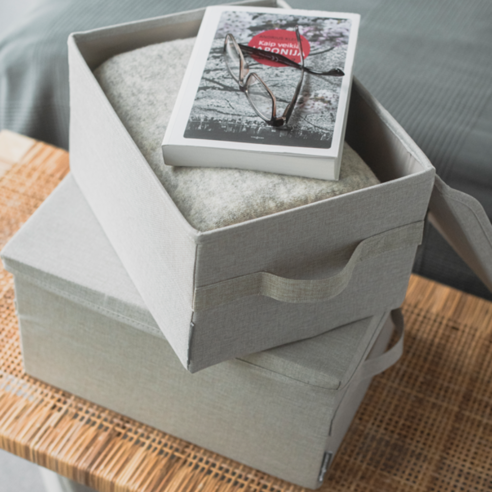 Twee Bigso SOFT opbergboxen in beige (40x30x22 cm) staan op elkaar op een gevlochten ondergrond. De bovenste box is open; daarin liggen een deken, een boek en een bril.