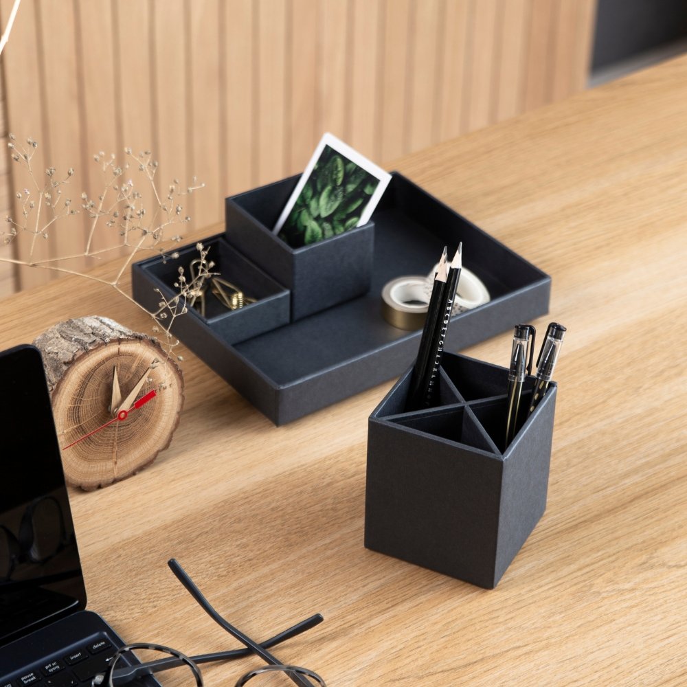 Pennenbakje met pennen en pennenhouder op een houten bureau naast een laptop.