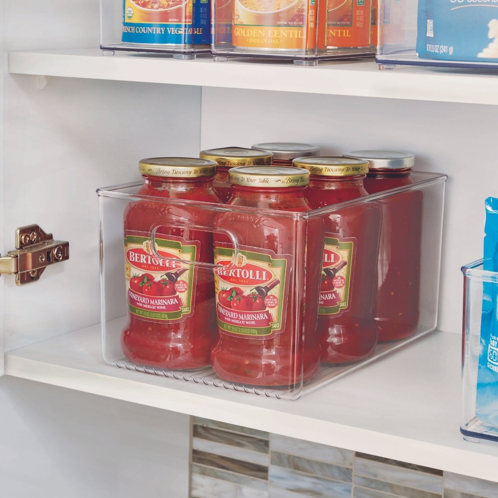 Potten met tomatensaus staan in een doorzichtige bak op een plank in de keukenkast.